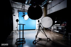 Interior of modern spacious photo studio with hanging blue background spotlight and laptop before shooting